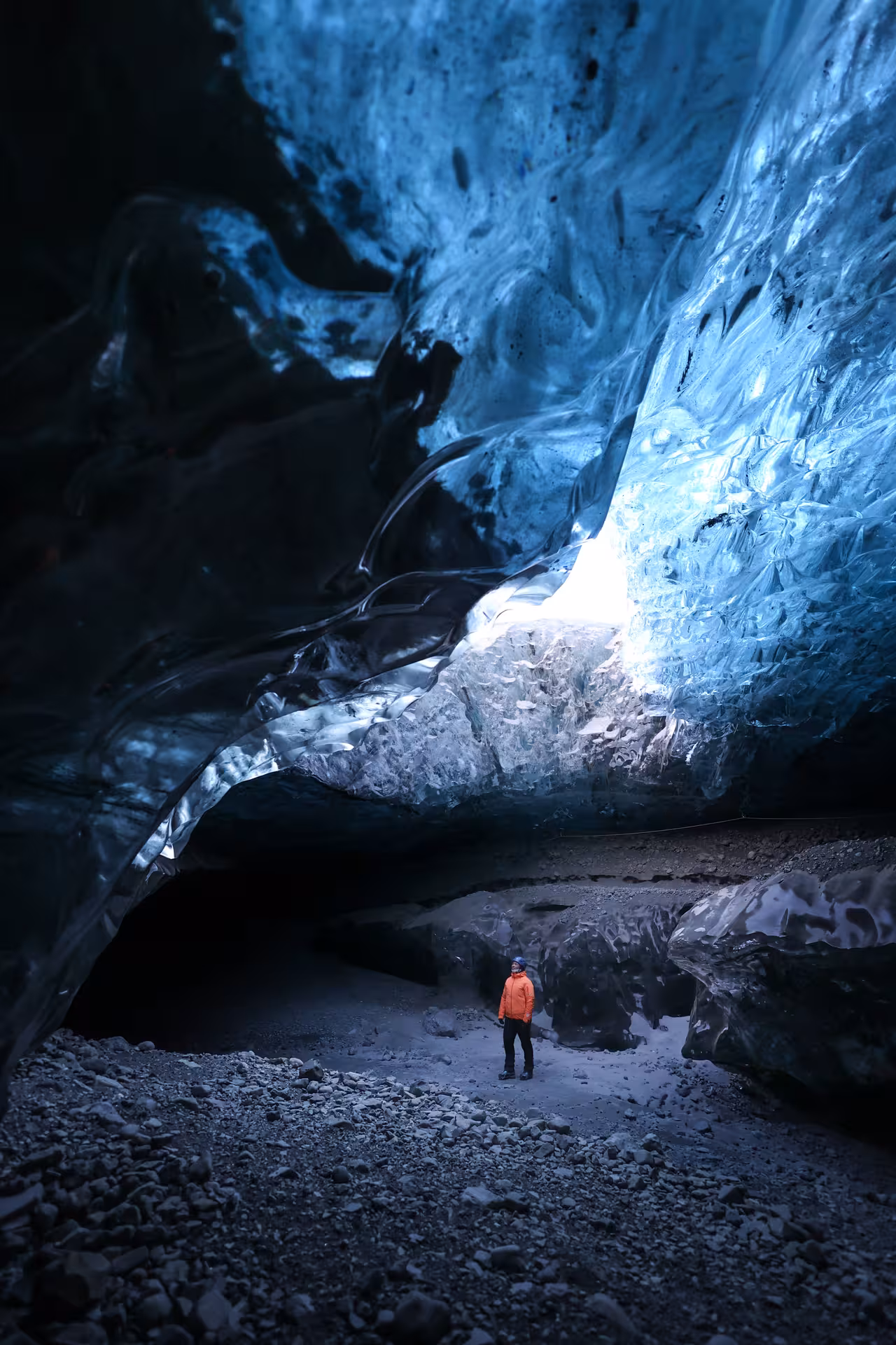 Explorer in orange jacket marvels at glowing blue glacial ice cave walls on an Iceland winter glacier adventure tour.