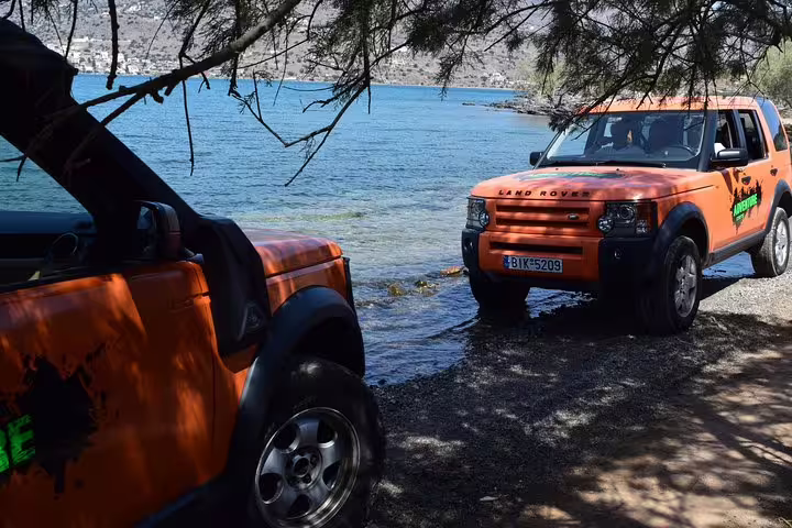 Bright orange Land Rovers parked by the serene waters of Spinalonga Island, ideal for adventurous Crete tours.