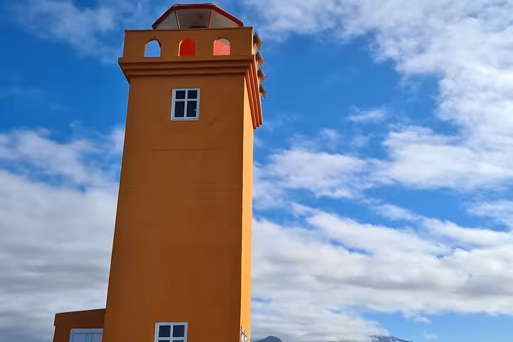 Tall orange lighthouse tower with red lantern room against blue sky on Snaefellsnes Peninsula