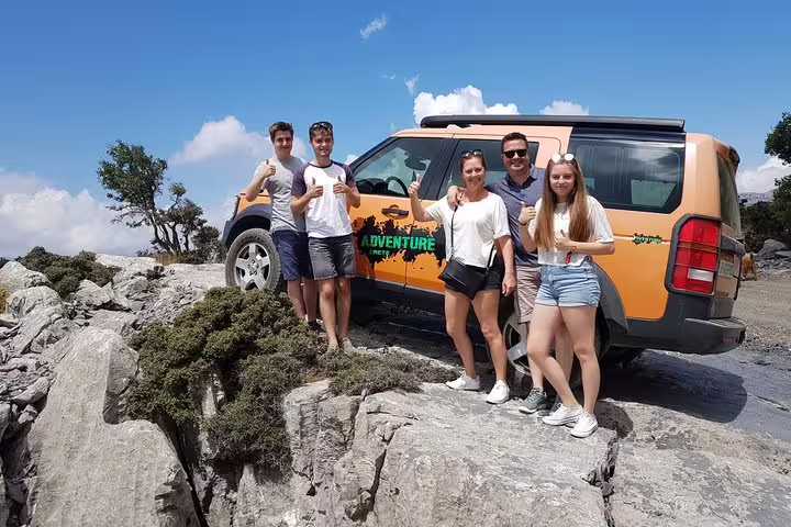 Group enjoying an off-road adventure near Azoria, standing beside an orange SUV with stunning North Coast views.