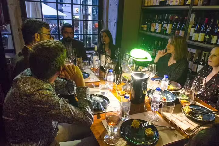 Group enjoying natural and organic wine tasting with gourmet food pairings in cozy, ambient setting for unique culinary experience.
