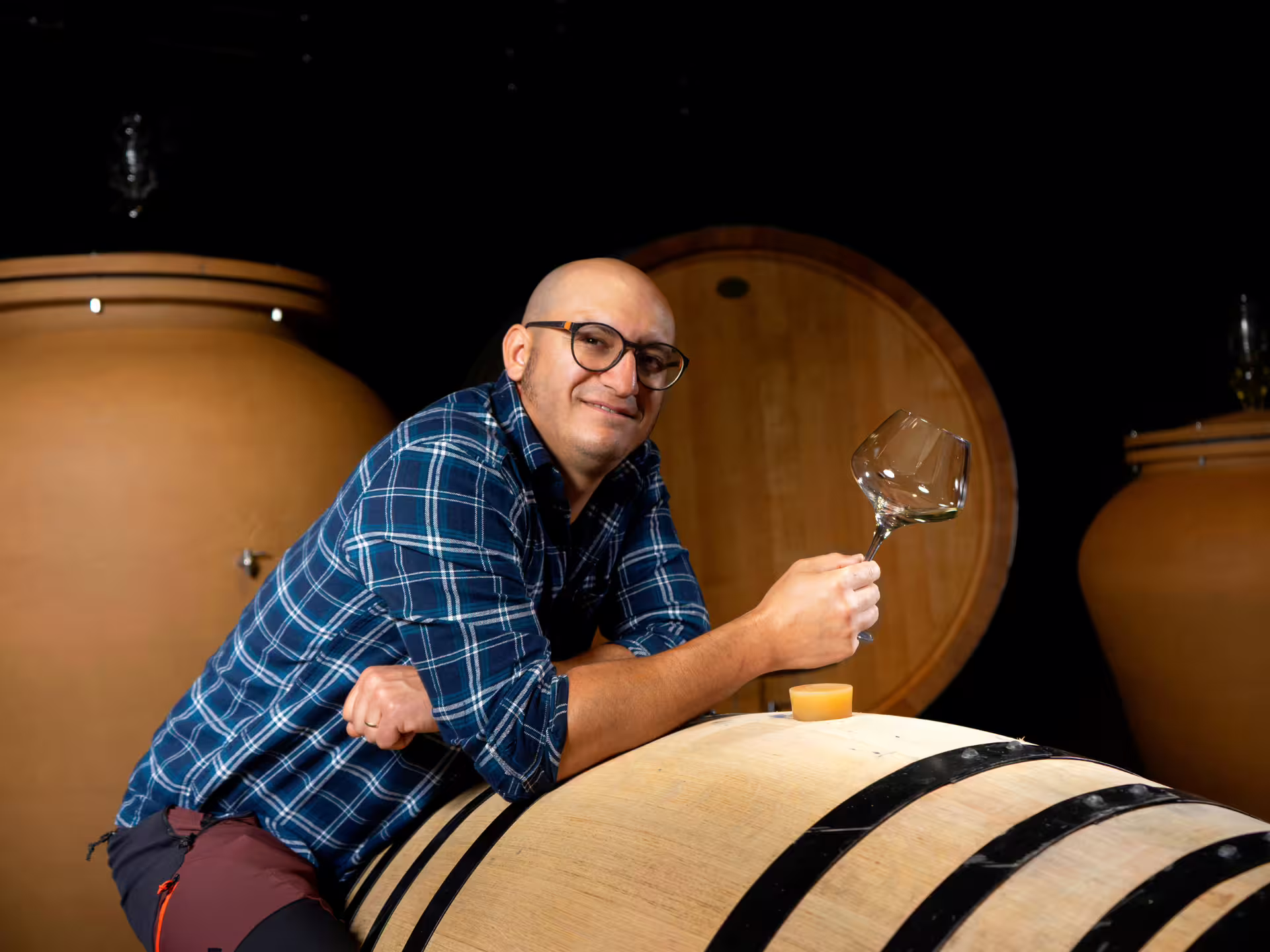 Winemaker in cellar holding wine glass beside barrel during organic winery visit near Turin with food pairing