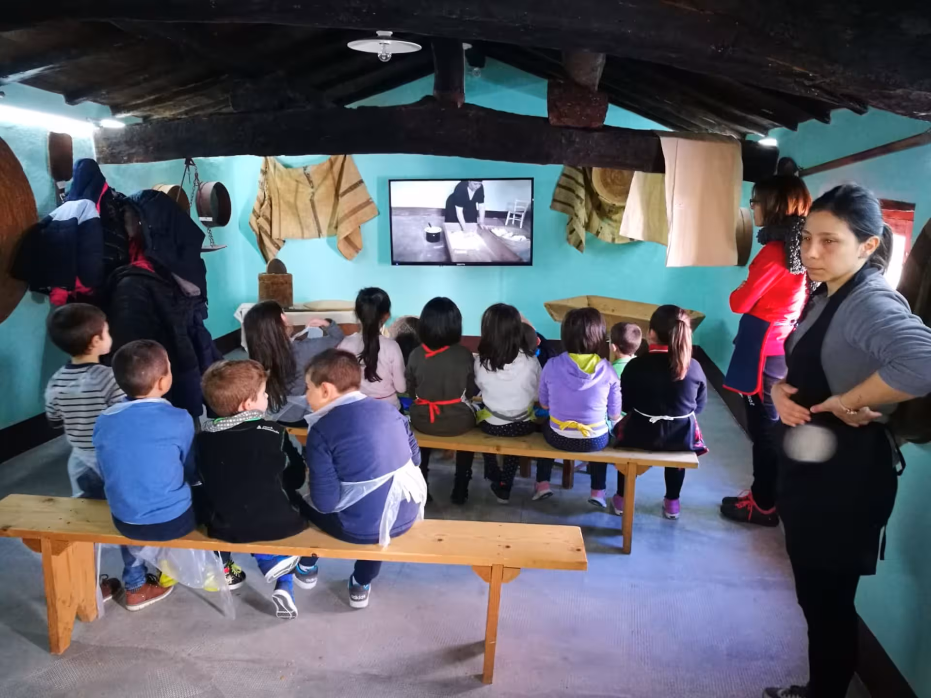 A group of children sits on benches watching an educational video at the Bread Museum in Orgosolo.