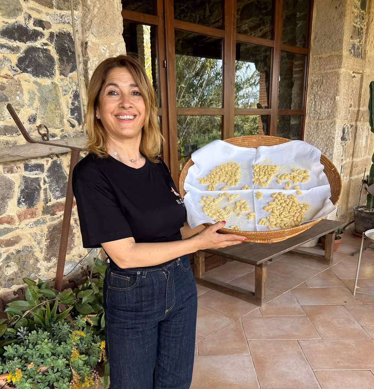 Smiling woman holding homemade pasta tray at Oristano's authentic pasta-making workshop.