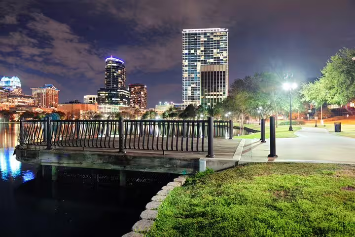 Downtown Orlando skyline at night viewed from a lakeside park walkway with glowing city lights