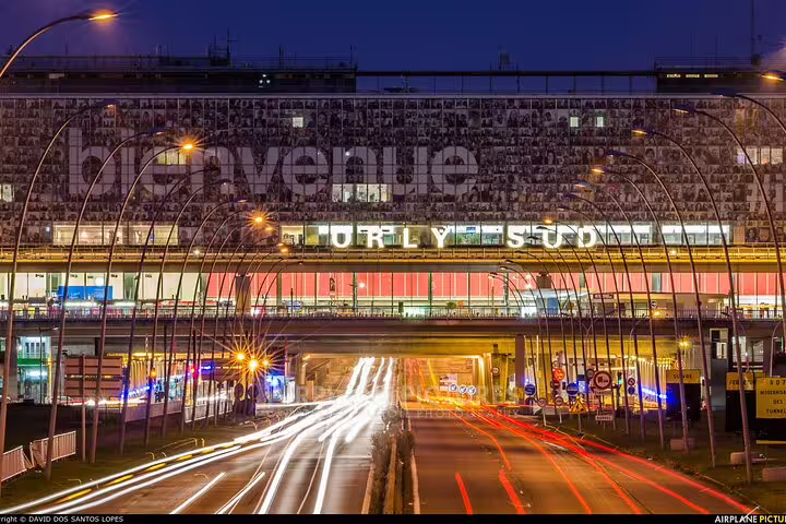 Orly Sud terminal entrance at night with traffic light trails, meet-and-greet private transfer to Paris