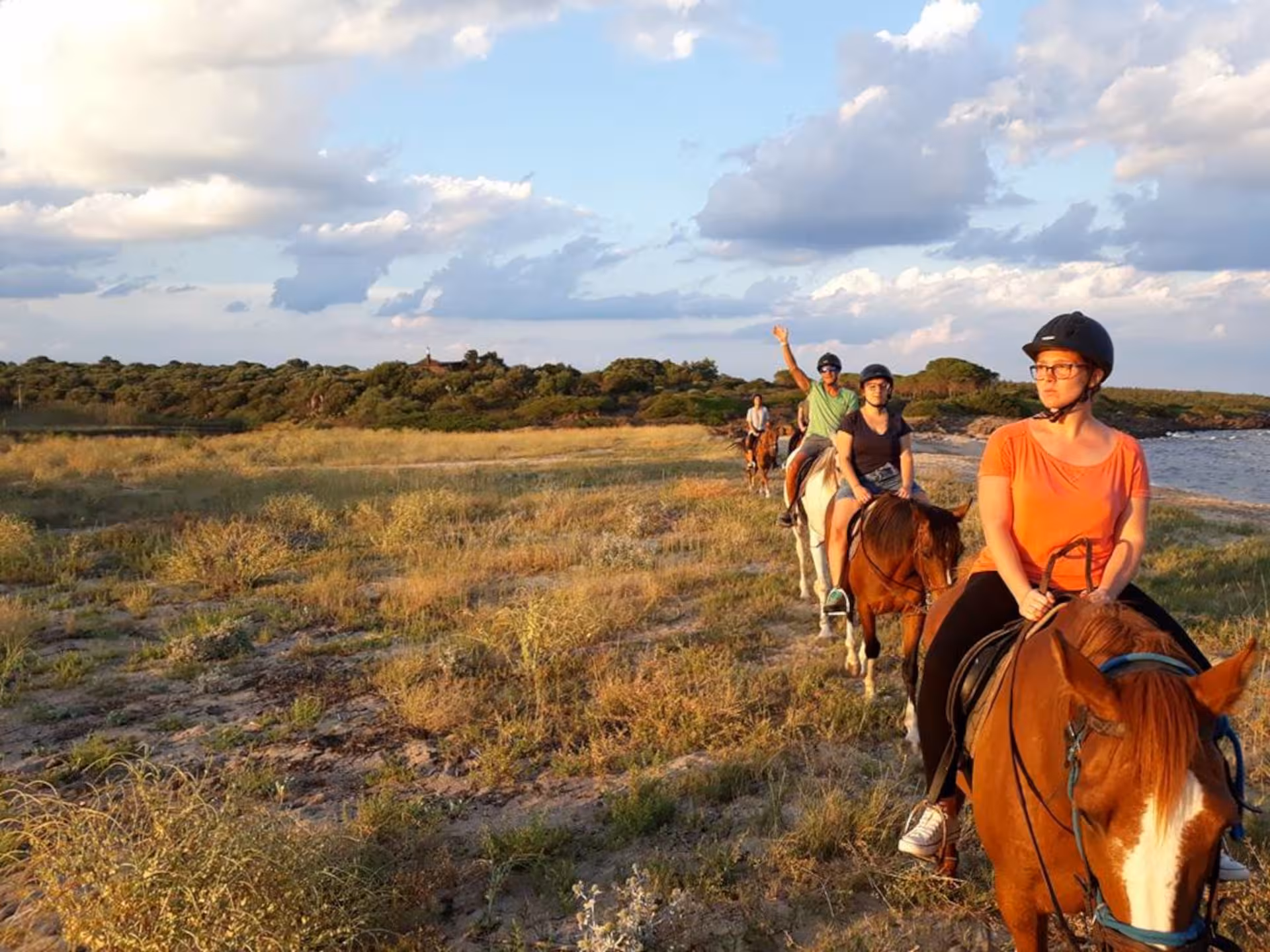 Group enjoying horse riding along Orosei beach at sunrise, surrounded by scenic coastal views and lush greenery.