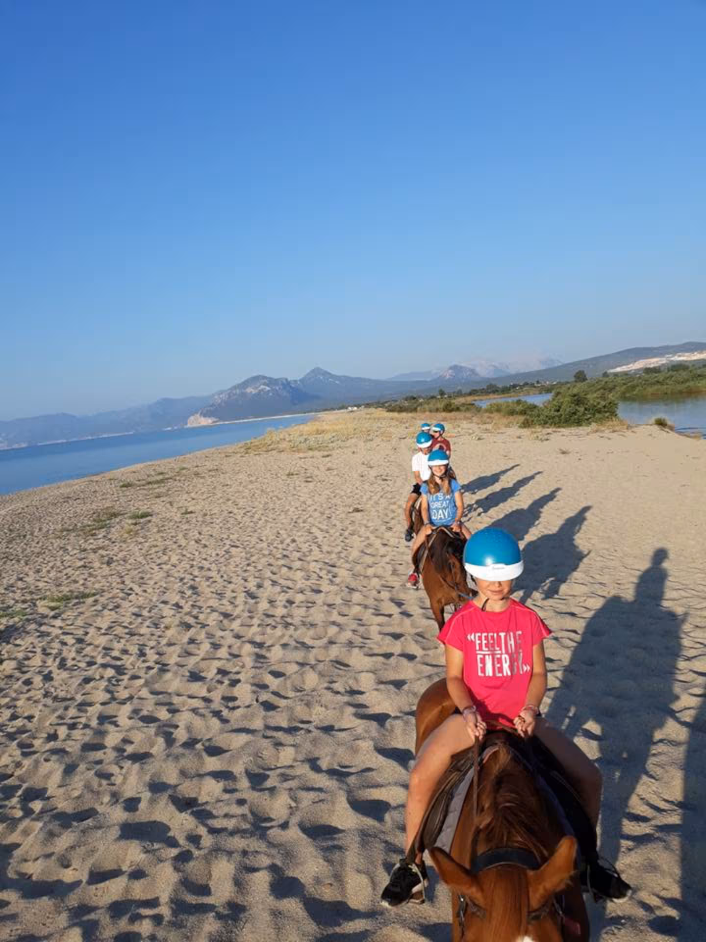Children enjoying a scenic horseback ride on Orosei beach at sunrise, with mountains in the background.