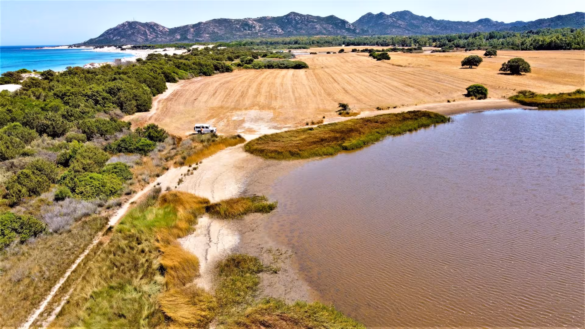 Aerial view of a jeep parked near Capo Comino, showcasing scenic landscapes with coastal fields and azure waters.