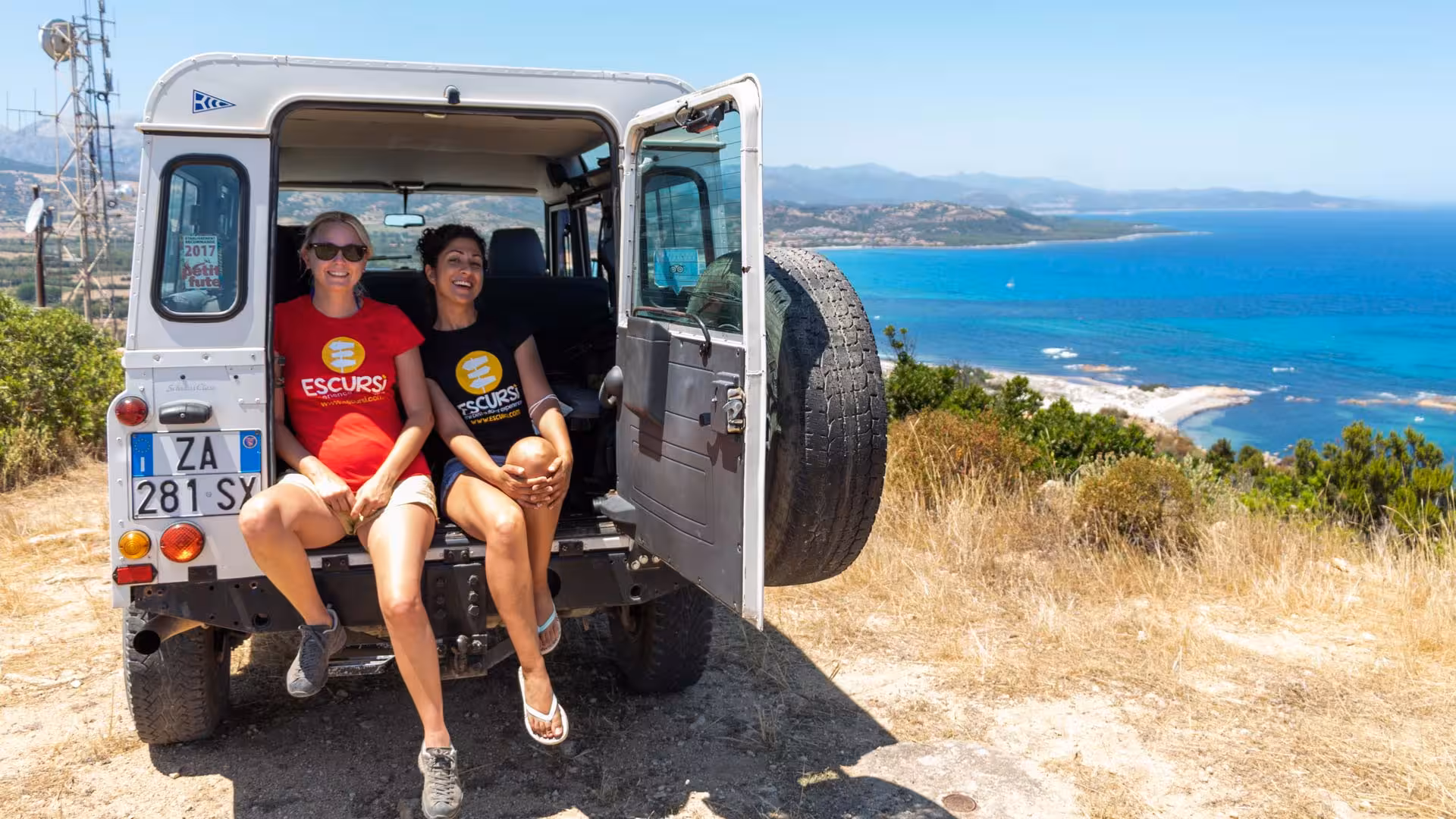 Tour participants enjoying a break in a Jeep overlooking Capo Comino's scenic coastline, showcasing Orosei's natural beauty.