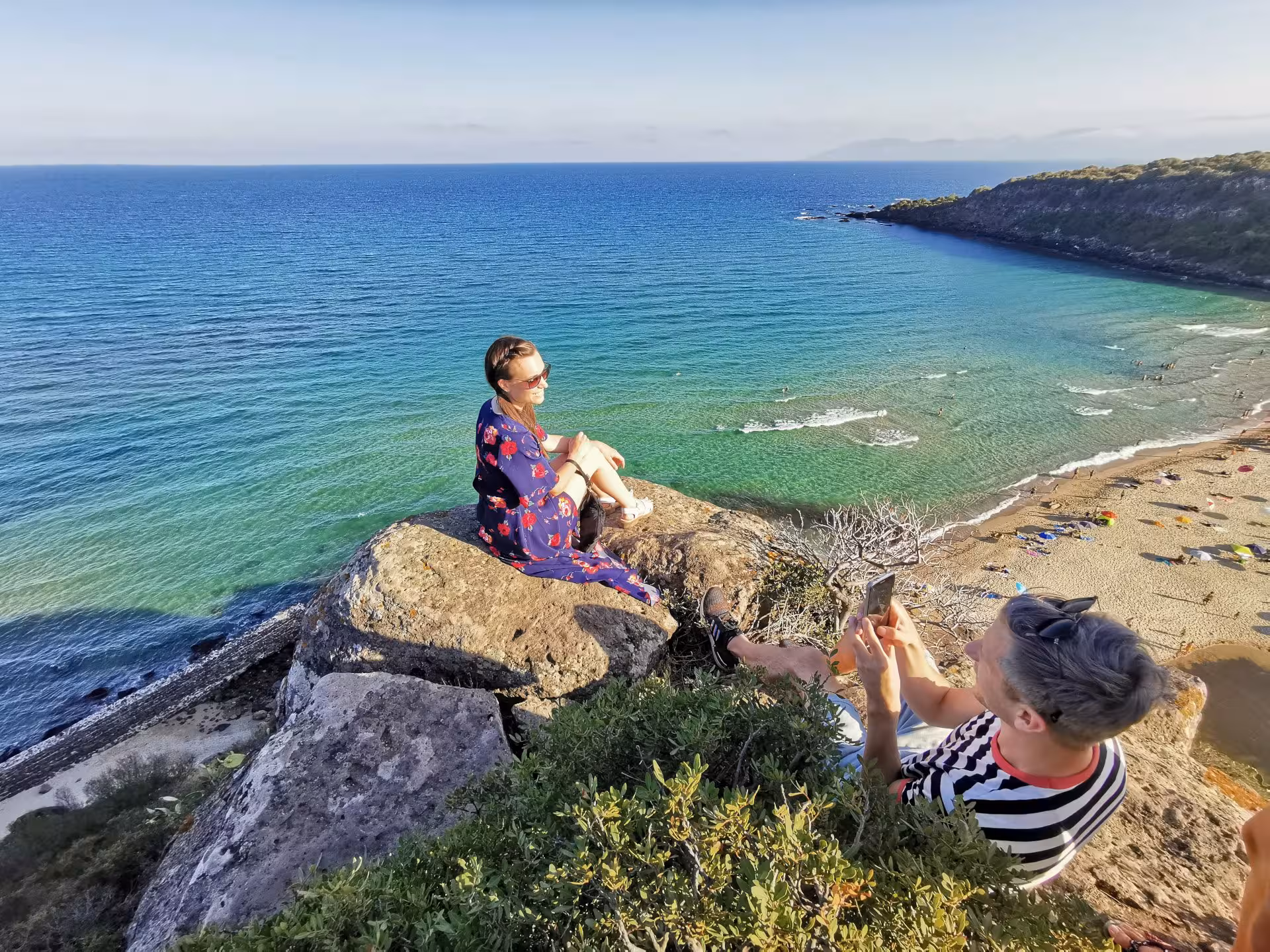 Tourists enjoy stunning coastal views from a cliff in Orosei, Sardinia, highlighting scenic beauty and adventure.