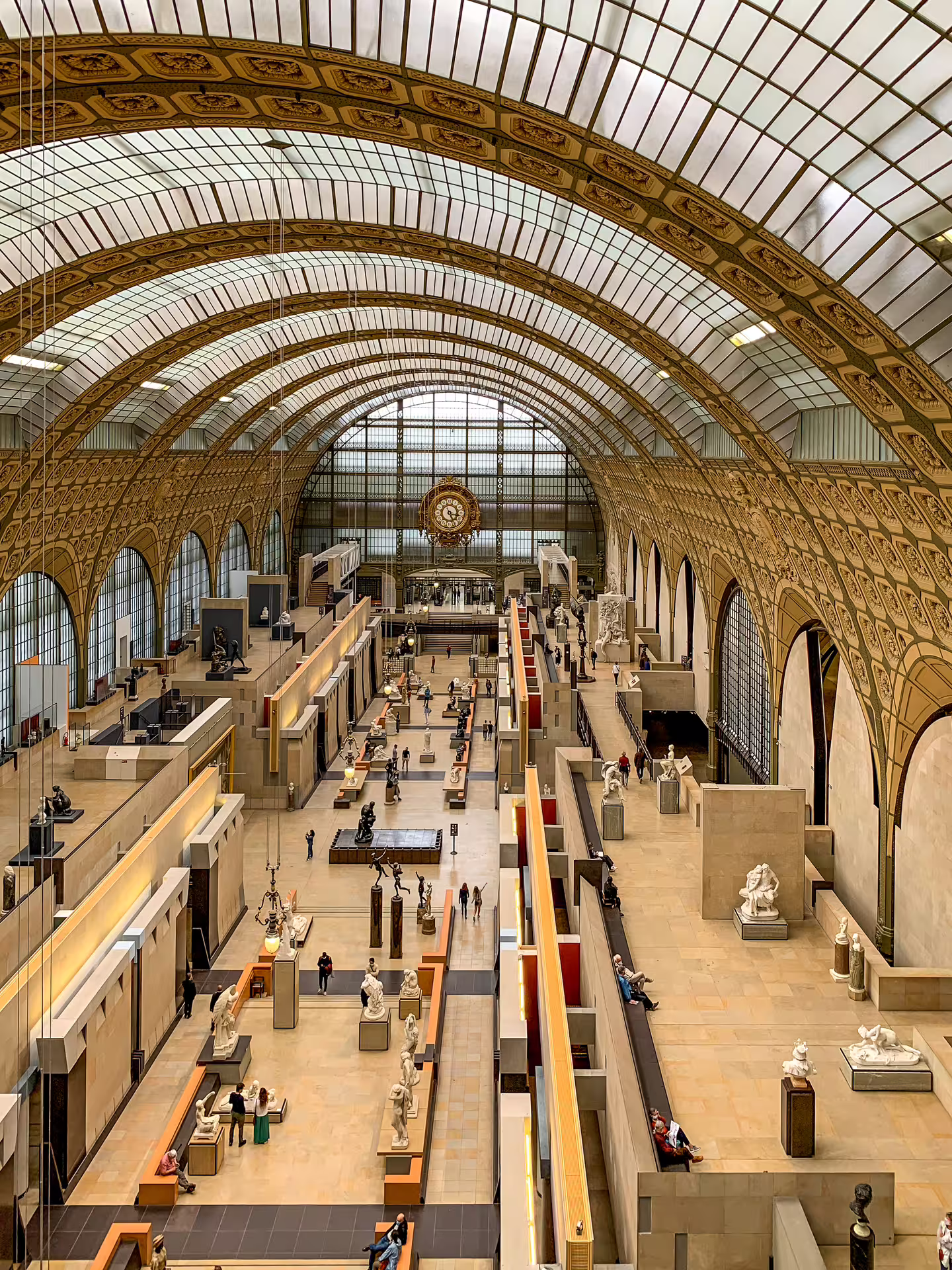 Grand hall of Musée d'Orsay with vaulted glass ceiling, sculptures, and large ornate clock