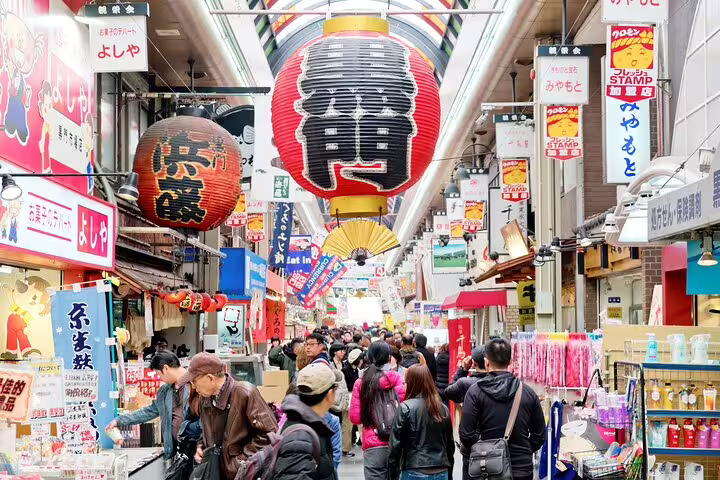 Crowded Osaka market street with red Japanese lanterns and colorful shop signs overhead