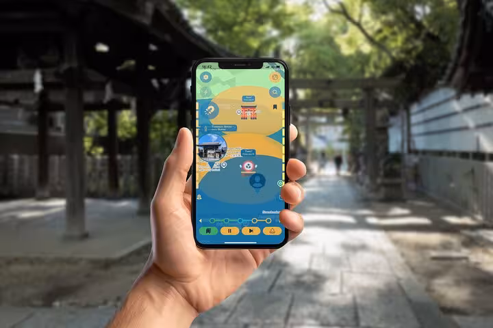 Hand holding smartphone displaying self-guided walking tour app at Japanese shrine pathway in Osaka