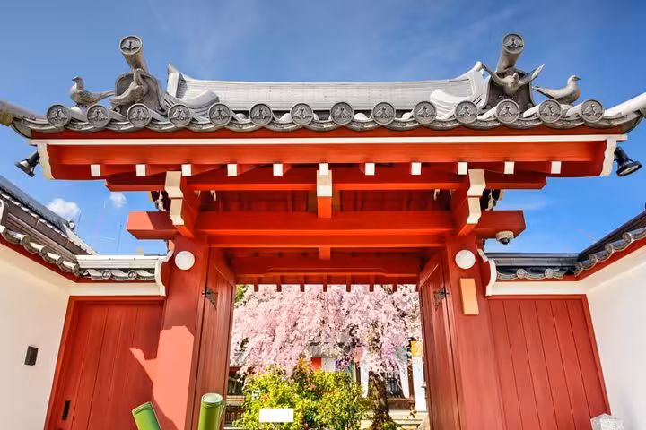 Red traditional Japanese gate with ornate tiled roof and cherry blossoms in Osaka