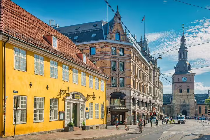 Historic Oslo street with yellow building, grand architecture, and church tower on sunny day