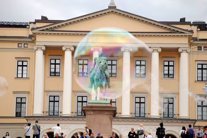 Large soap bubble floating in front of Oslo Royal Palace equestrian statue with tourists below