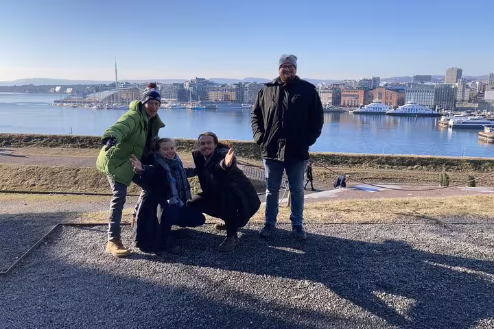 Four tourists posing at Oslo harbor viewpoint with city skyline and fjord in background
