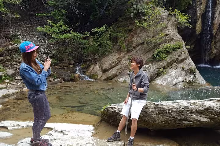 Visitors enjoying a scenic moment by the tranquil waters of Bogove Waterfall in the lush Osum Canyon.