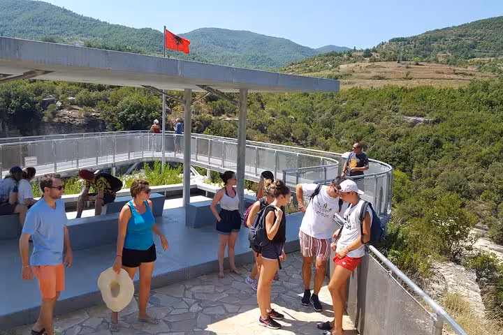 Visitors enjoy the scenic viewpoint over Osum Canyon with lush greenery and an Albanian flag in the background.