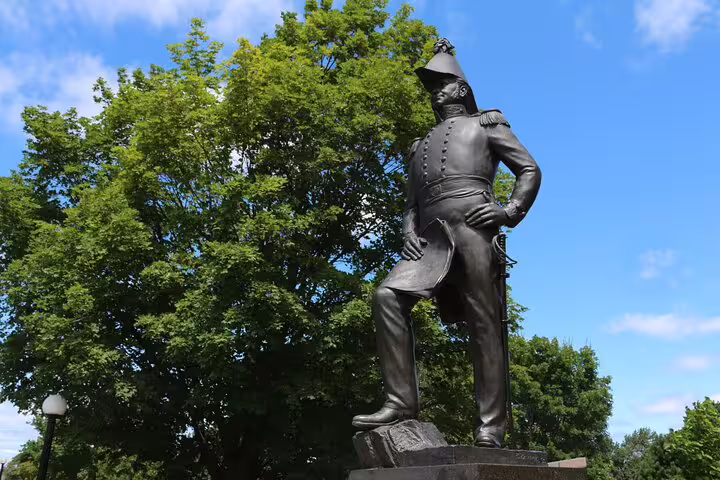 Bronze military statue on pedestal surrounded by green trees in Ottawa city park