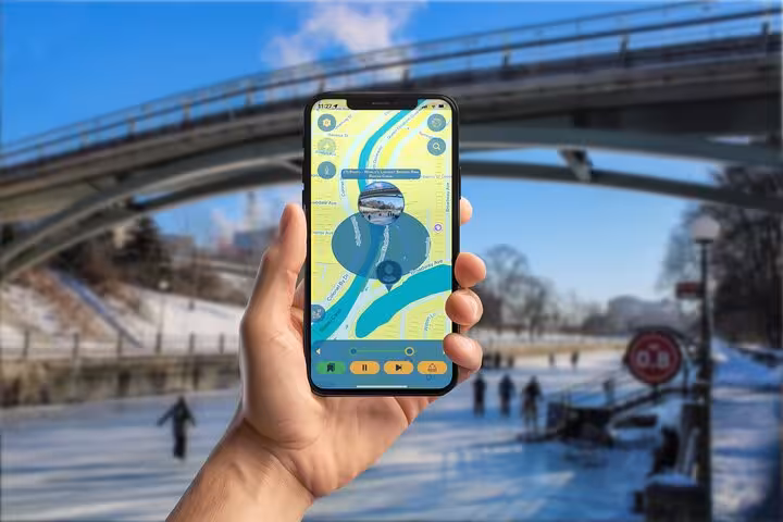 Hand holding smartphone with scavenger hunt app map near Ottawa canal bridge in winter