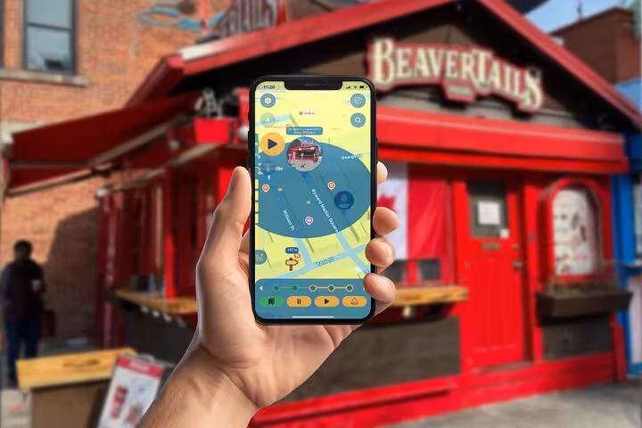 Hand holding smartphone with scavenger hunt app map in front of BeaverTails shop in Ottawa