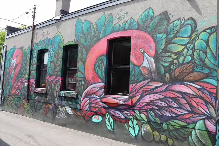 Vibrant flamingo street art mural with tropical leaves on a grey building wall in Ottawa