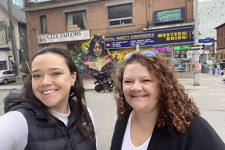 Two women smiling on a street in Ottawa with colorful murals and storefronts in the background