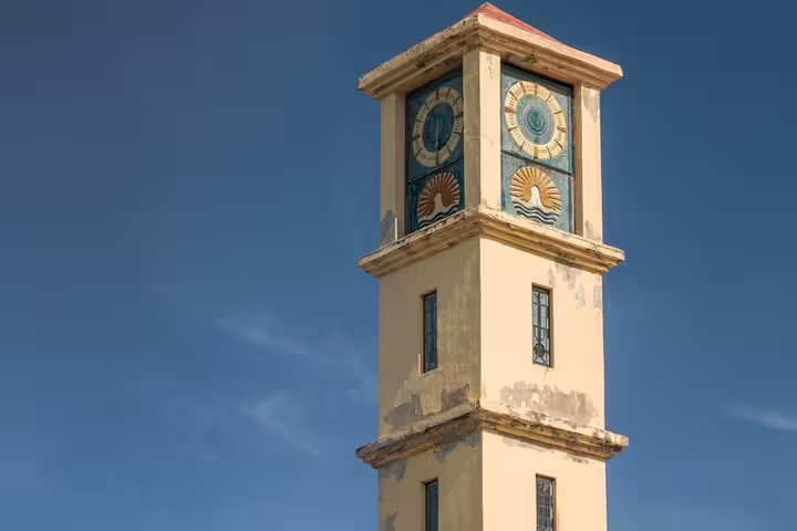 Historic Ottoman clock tower with ornate blue clock faces against a clear blue sky in Kusadasi