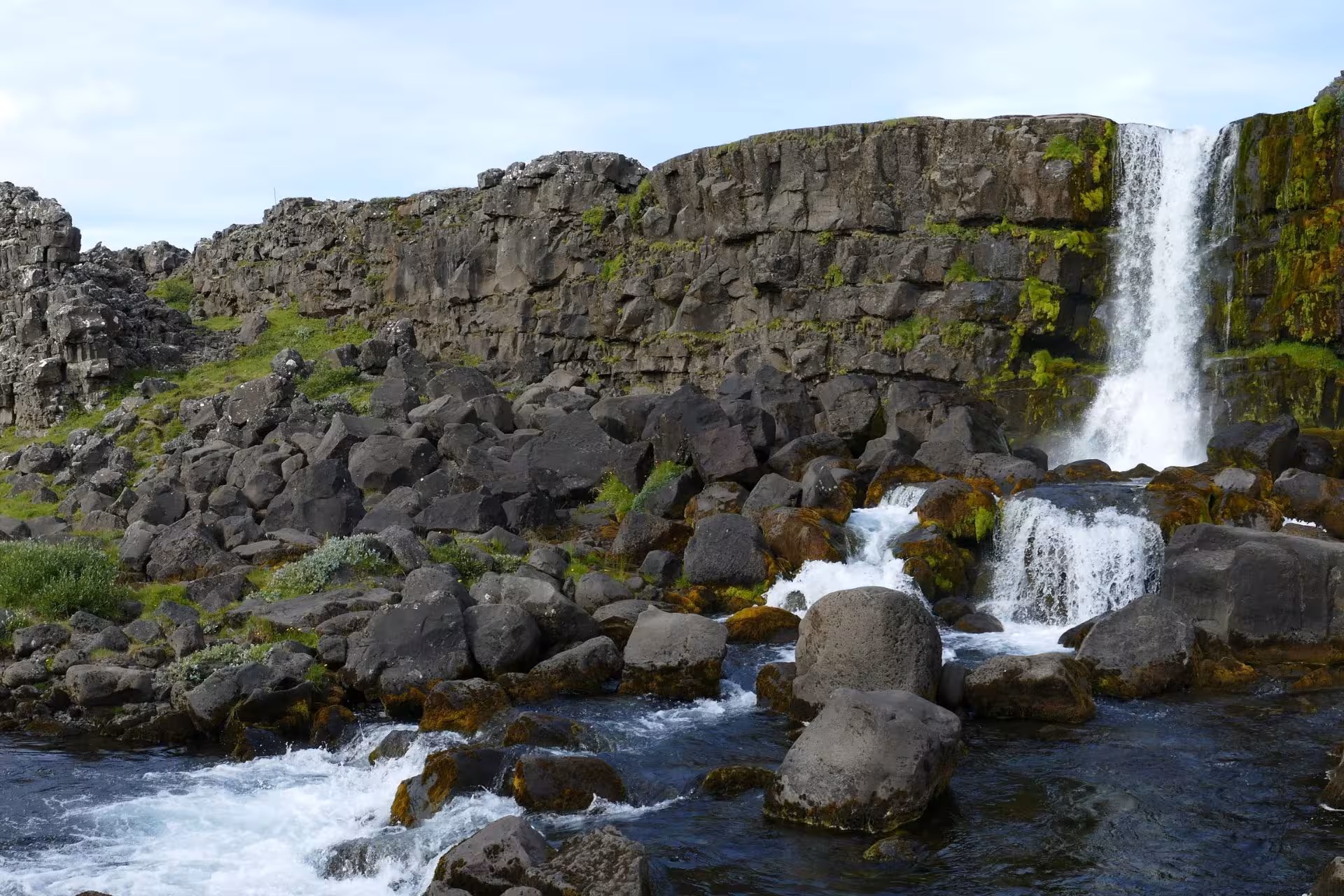 Öxará waterfall cascading over mossy basalt cliffs into rocky river at Þingvellir, Iceland
