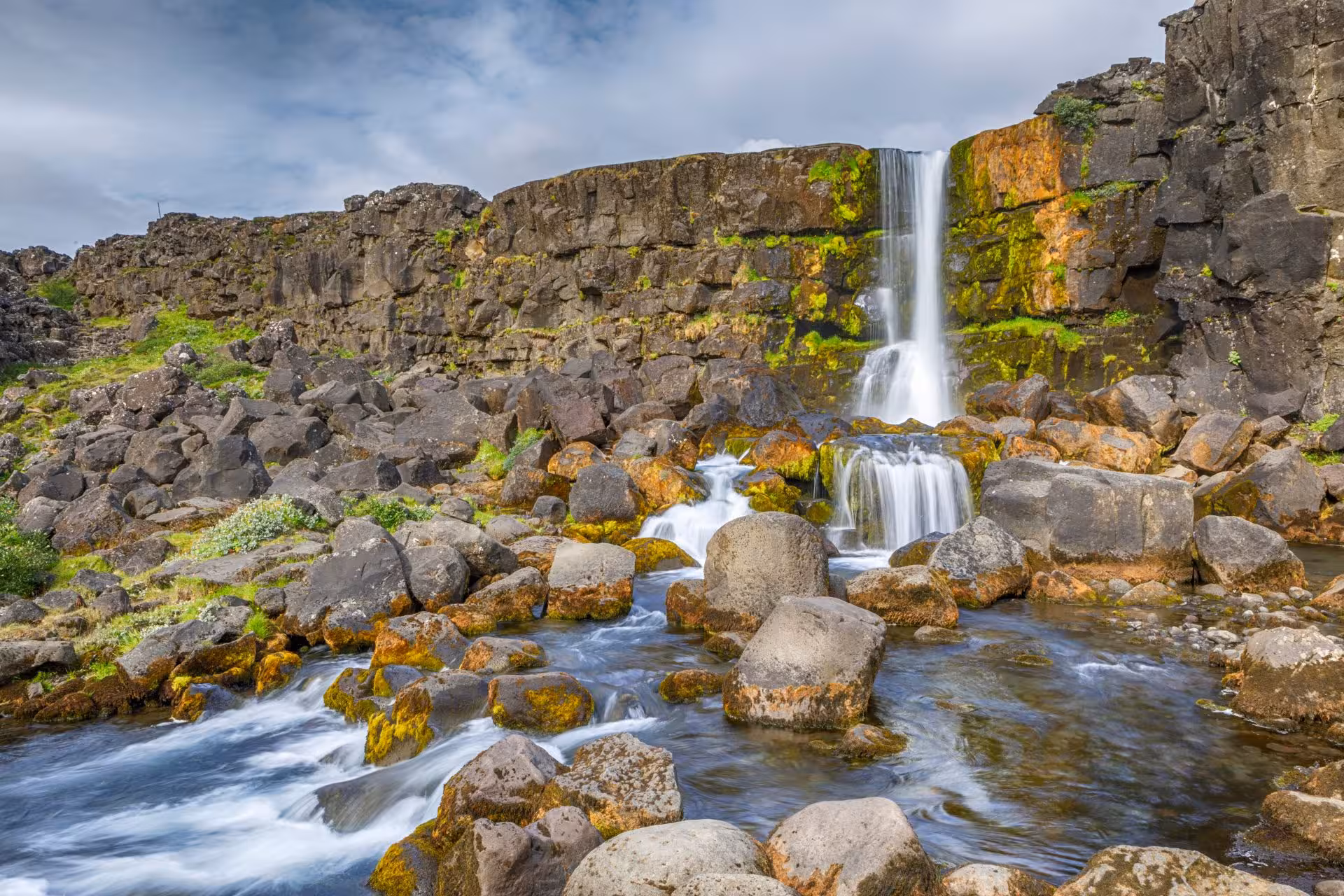 Öxará waterfall cascading over mossy basalt cliffs into rocky stream at Þingvellir, Iceland
