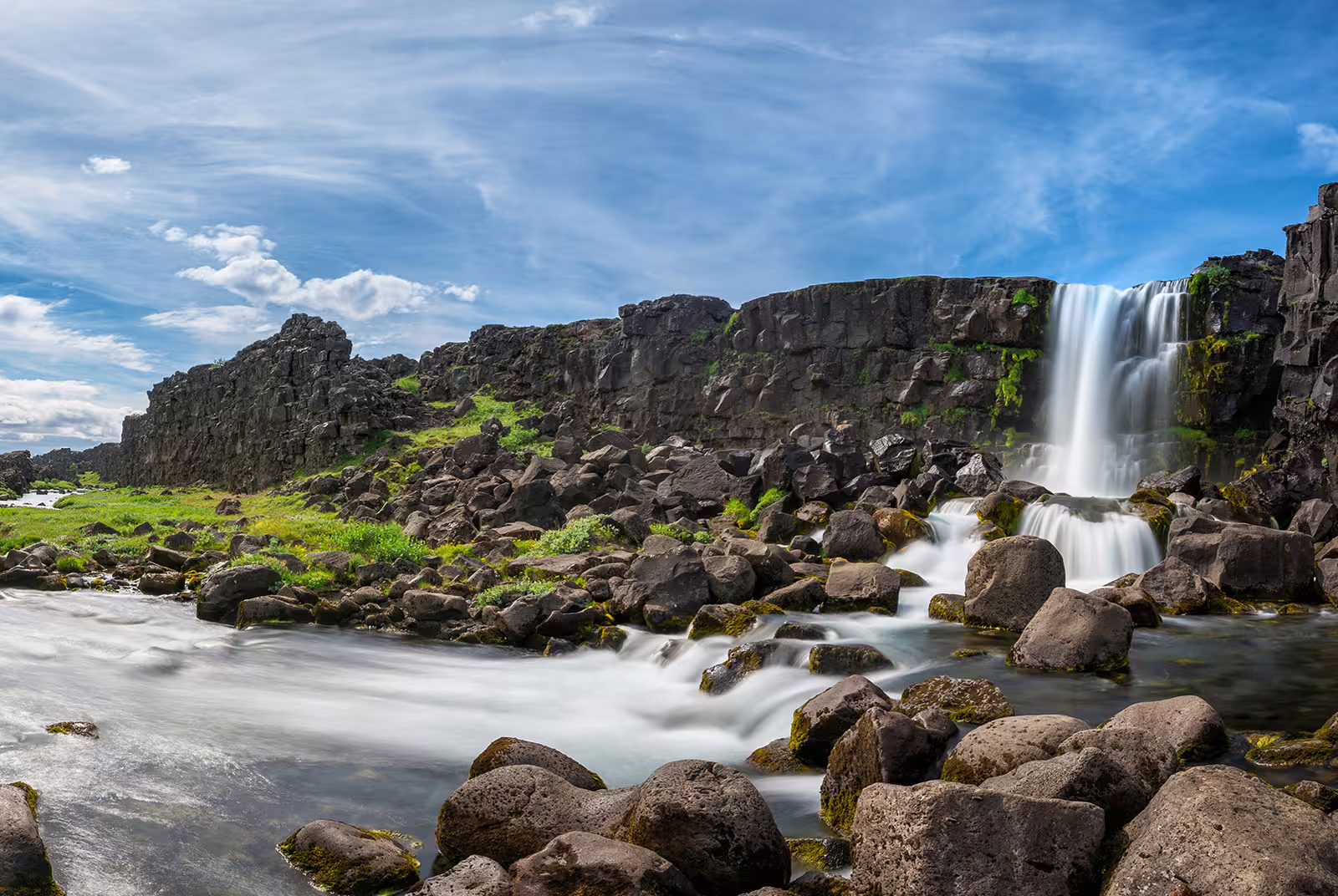 Öxará waterfall cascading over dark lava rock cliffs into a rocky river in Iceland's Þingvellir National Park