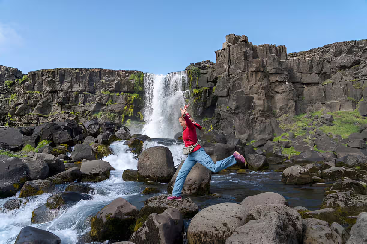 Traveler jumping on rocks at Öxará waterfall, Þingvellir National Park, Golden Circle Iceland