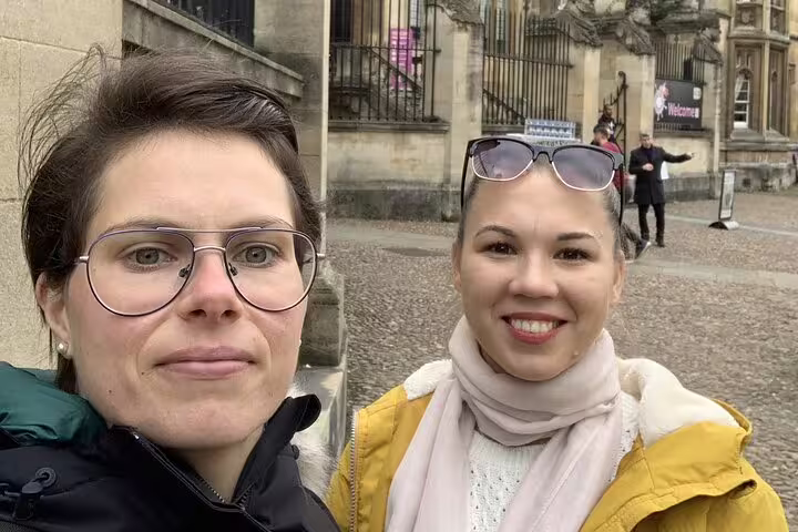 Two women smiling on a cobblestone street outside historic Oxford university buildings