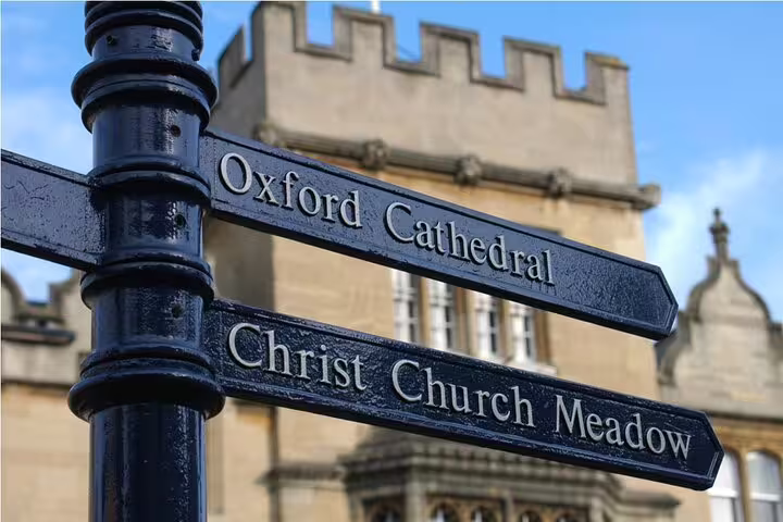 Directional signpost pointing to Oxford Cathedral and Christ Church Meadow with historic building behind