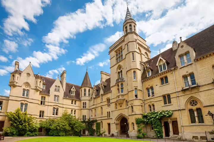 Gothic stone courtyard of an Oxford college with tower, spires, and green lawn under blue sky