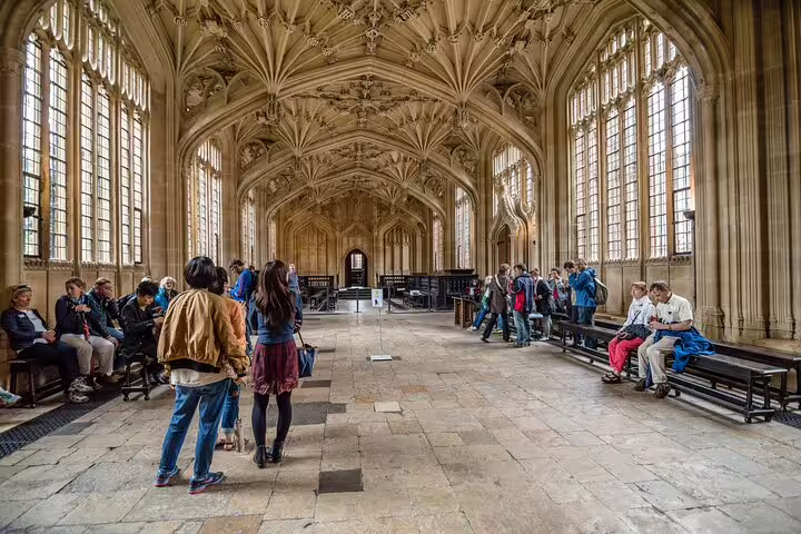 Tourists explore the stunning vaulted ceiling and historic architecture of Oxford's Divinity School on a day trip from London.