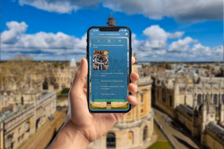 Hand holding smartphone with Oxford self-guided tour app showing quiz question, Radcliffe Camera visible in background