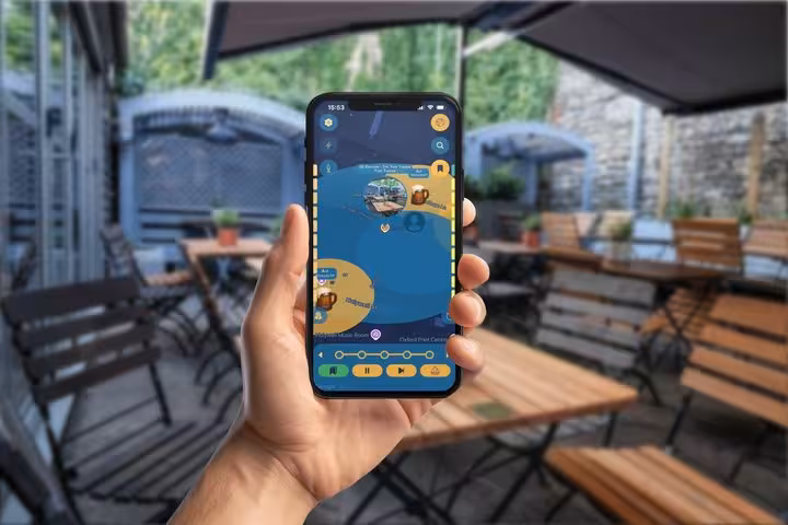 Hand holding smartphone displaying Oxford self-guided walking tour GPS app with blue and yellow map interface