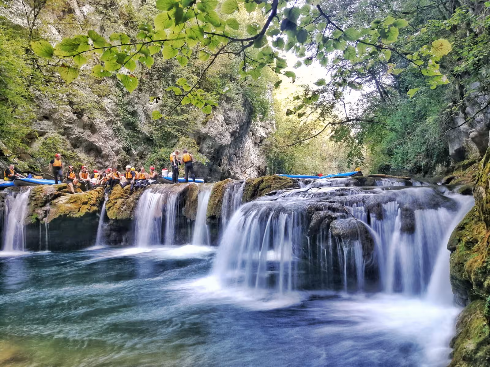 Group of kayakers resting on rocks by cascading waterfalls in scenic Mreznica Canyon, Croatia, amidst vibrant nature.