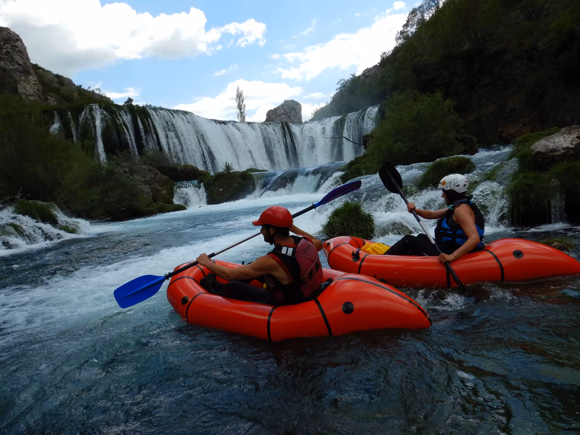 Two adventurers packrafting on the scenic Zrmanja River near cascading waterfalls, perfect for outdoor enthusiasts.