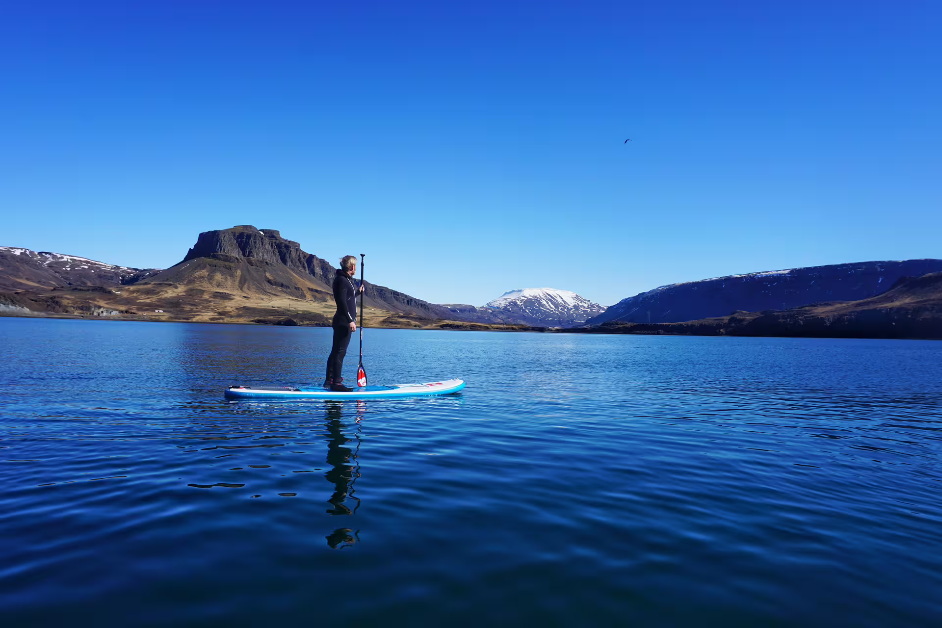 Paddle boarder navigates serene waters of the Forgotten Fjords, surrounded by majestic cliffs and clear blue skies.
