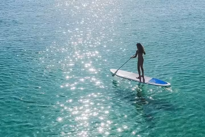 Solo paddleboarder standing on crystal-clear turquoise water, exploring Albufeira coast with stand up paddle rental