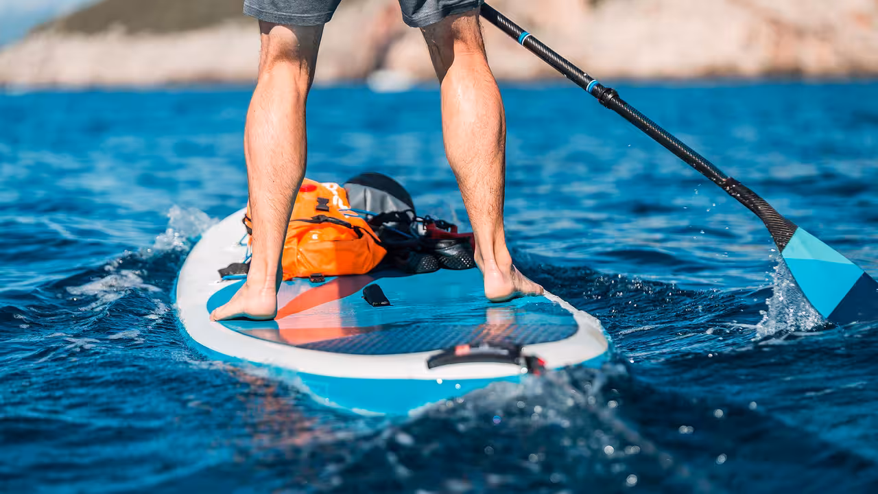 Close-up of paddleboarder’s legs and gear gliding over turquoise Atlantic waves during SUP paddle rental in Albufeira