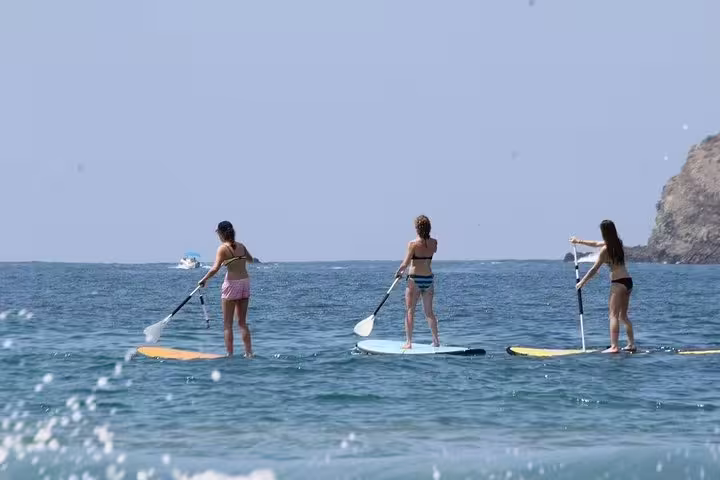 Three women paddleboarding together on the clear ocean waters of Manuel Antonio, Costa Rica, with scenic views.
