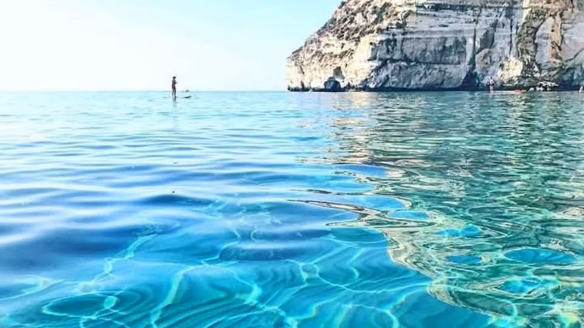 Paddleboarder enjoying the crystal-clear waters near rocky cliffs in the Gulf of Angels, Cagliari.