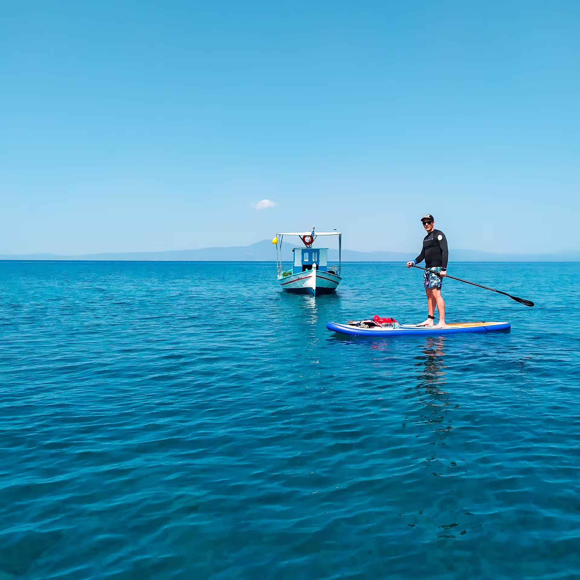 Paddleboarder on calm Kalamata sea with fishing boat ahead, enjoying a scenic SUP adventure in Greece
