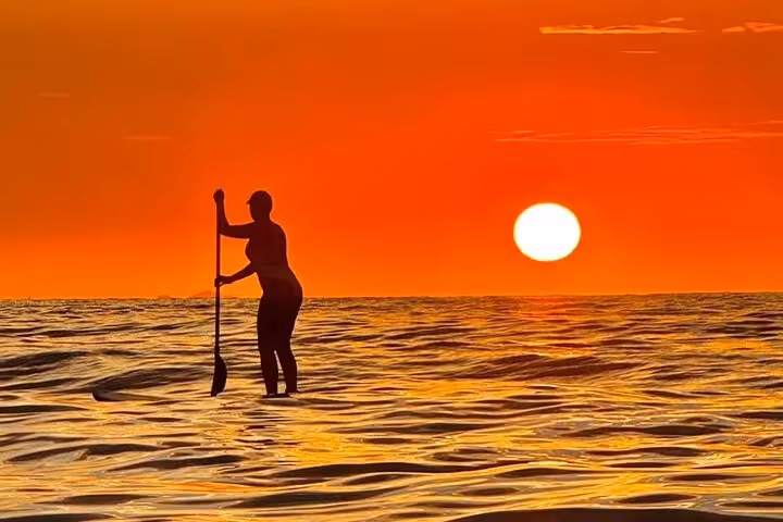 Silhouette of a paddleboarder at sunrise in Copacabana, capturing the serene beauty of a SUP tour on the river.