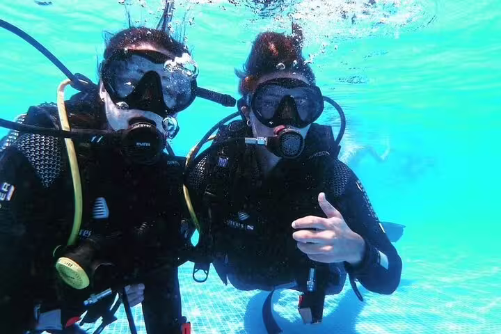 Two scuba divers in wetsuits and masks underwater during an open water course, showcasing excitement and adventure.